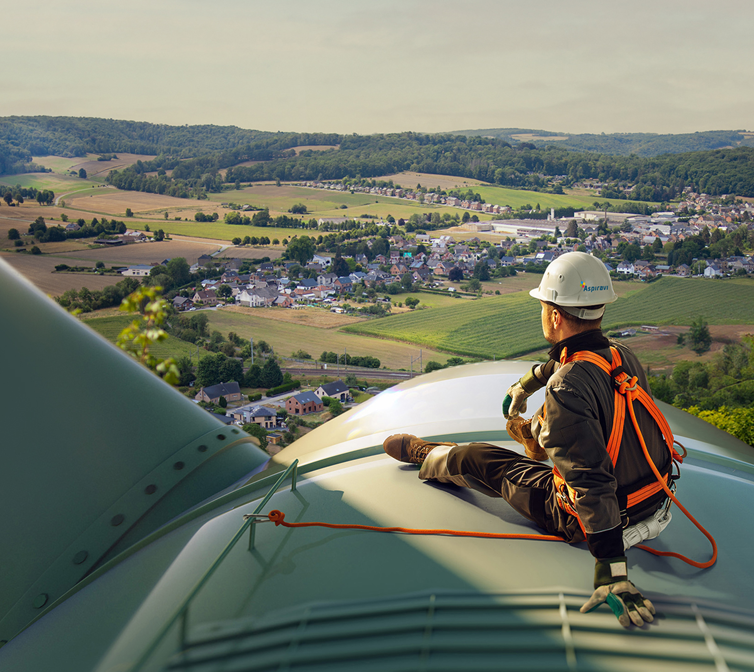 Technicus op een windturbine met uitzicht over velden en een dorp.